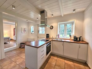 A modern kitchen with white cabinetry, a central island, a window with a view, and a built-in stove. - Ilskes Hus - Detached thatched house with garden, terrace & e-charging station (Oevenum)