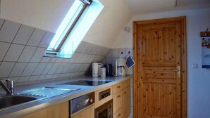 Una cocina con tragaluz, un lavamanos, una cafetera, armarios de madera y una puerta de madera.