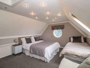 A bedroom with a sloped ceiling, a round window, two beds, and a nightstand.