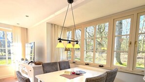 Un coin repas avec une table blanche, des chaises en osier et un luminaire suspendu.
