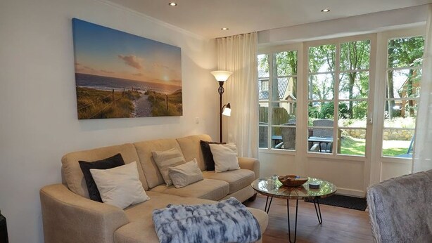 Un salon avec un canapé beige, une table basse en verre et un tableau représentant un coucher de soleil.