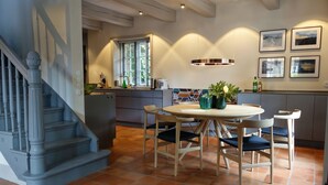 A modern kitchen with a dining area, featuring a staircase, a round table with chairs, and a view of the outside through a window. - Reethus main house on the ground floor/ first floor - Reethus in Borgsum: 121 m², sauna, fireplace & garden, (Borgsum)