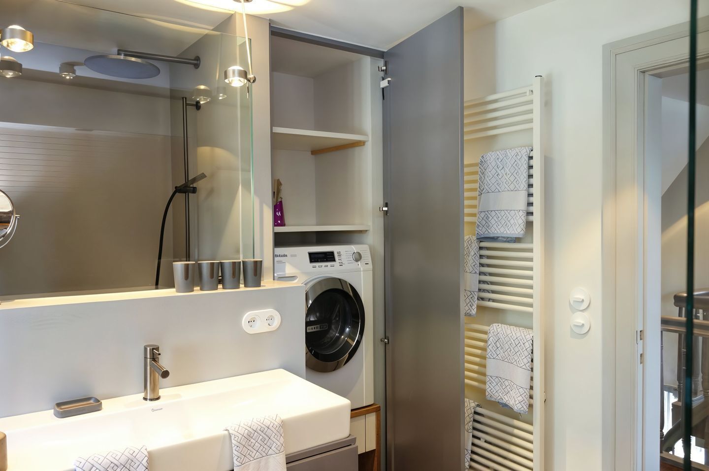 Une salle de bain moderne équipée d’un lave-linge intégré, d’un grand miroir et d’un porte-serviettes.
