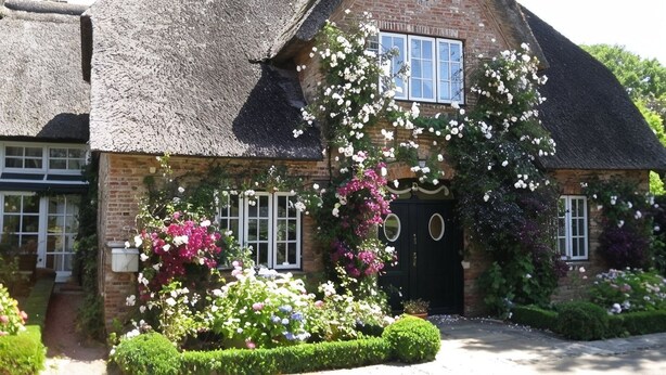 A traditional brick house with a thatched roof, a central window, and a door with a circular window above it. - Reethus main house on the ground floor/ first floor - Reethus in Borgsum: 121 m², sauna, fireplace & garden, (Borgsum)
