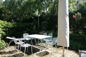 An outdoor patio with a white table and chairs, surrounded by greenery and a white umbrella. - Reethus main house on the ground floor/ first floor - Reethus in Borgsum: 121 m², sauna, fireplace & garden, (Borgsum)