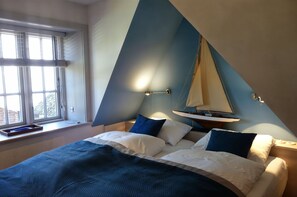 A bedroom with a bed, pillows, a window, and a sailboat model on the wall. - Reethus main house on the ground floor/ first floor - Reethus in Borgsum: 121 m², sauna, fireplace & garden, (Borgsum)