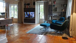 A living room with a television, a blue sofa, a coffee table, and a bookshelf. - Reethus main house on the ground floor/ first floor - Reethus in Borgsum: 121 m², sauna, fireplace & garden, (Borgsum)