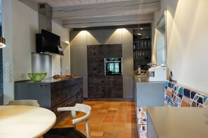Eine kompakte Küche mit Einbauofen, Mikrowelle und Kaffeemaschine. Es gibt einen Essbereich mit Tisch und Stühlen.