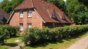 A two-story brick house with a sloped roof, multiple windows, and a garden with pink flowers. - Godewind - Apartment 1 - Holiday apartment Godewind 1: first floor with terrace, WLAN (Wyk auf Föhr)