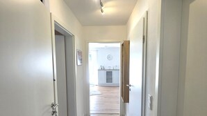 A hallway with white walls and wooden flooring leading to a room with a clock and a small table. - Godewind - Apartment 1 - Holiday apartment Godewind 1: first floor with terrace, WLAN (Wyk auf Föhr)