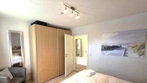 A bedroom with a bed, a chair, a wardrobe, and a painting on the wall. - Godewind - Apartment 1 - Holiday apartment Godewind 1: first floor with terrace, WLAN (Wyk auf Föhr)