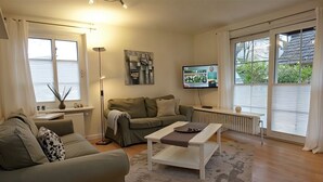 A living room with a sofa, a coffee table, a floor lamp, a TV, and a radiator. - Godewind - Apartment 1 - Holiday apartment Godewind 1: first floor with terrace, WLAN (Wyk auf Föhr)