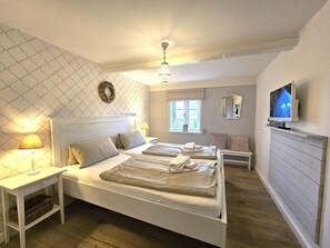 Ein Schlafzimmer mit zwei Betten, einem Fernseher, einem Fenster und einem Deckenventilator.