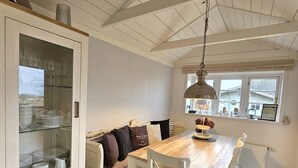 A cozy kitchen with a wooden table, white chairs, a glass cabinet, and a hanging light fixture. - WattGut - WattGut vacation home in Oevenum: sauna, wood-burning stove & garden for 6 guests (Oevenum)
