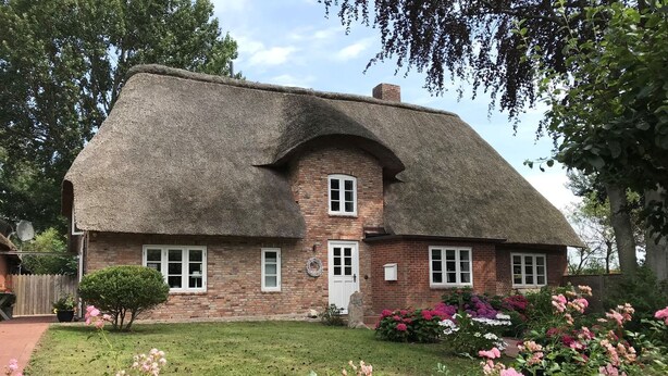 A traditional brick house with a thatched roof, a small front garden with pink flowers, and a brick chimney. - WattGut - WattGut vacation home in Oevenum: sauna, wood-burning stove & garden for 6 guests (Oevenum)