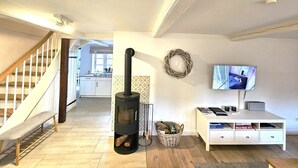 A modern living room with a fireplace, a TV, a white cabinet, and a staircase leading to another room. - WattGut - WattGut vacation home in Oevenum: sauna, wood-burning stove & garden for 6 guests (Oevenum)