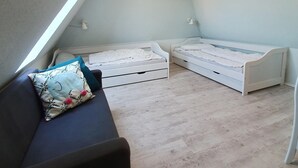 Ein Schlafzimmer mit schrägem Dach, zwei Einzelbetten, einer Schlafcouch und einem kleinen Tisch.
