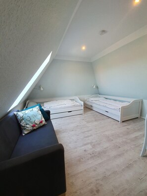 A bedroom with a sloped ceiling, two single beds, a sofa, and a small table. - Nis Puk - FW Oland - Space for up to 5 people, WLAN & 500 m to the beach (Utersum)