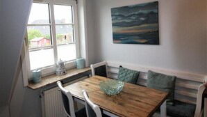 Ein Essbereich mit einem Holztisch, weißen Stühlen, einer Bank, einem Fenster mit Aussicht und einem Gemälde an der Wand.