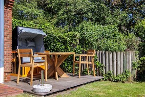 A patio with a wooden table and chairs, a covered seating area, and a brick wall. - Nis Puk _FW Gröde (ground floor) - Apartment Gröde on the ground floor in Utersum - Terrace & 500 m (Utersum)