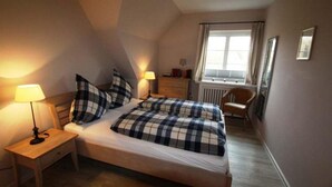 A bedroom with a bed, two bedside tables, a lamp, a chair, and a window. - Bredland 11 - Whg. 4 - Holiday apartment by the sea in Nieblum: Terrace, garden & 200 (Nieblum)