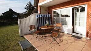 A patio with a table and chairs, a white fence, and a house in the background. - Bredland 11 - Whg. 4 - Holiday apartment by the sea in Nieblum: Terrace, garden & 200 (Nieblum)