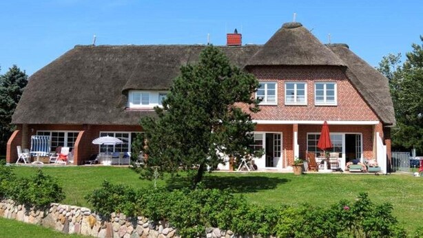 A house with a thatched roof, brick walls, and a well-maintained lawn. - Bredland 11 - Whg. 4 - Holiday apartment by the sea in Nieblum: Terrace, garden & 200 (Nieblum)