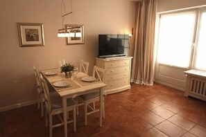 Ein Essbereich mit einem Tisch für vier Personen, einem Fernseher auf einem Schrank und einem Fenster mit Vorhängen.