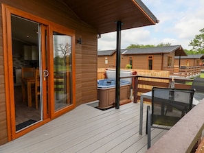 A wooden deck with a glass door leading to a room, a hot tub, and a table with chairs.