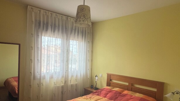 Un dormitorio con cama, mesita de noche, lámpara, espejo y ventana con cortinas.