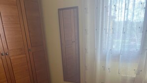 Un dormitorio con cama, armario de madera y ventana con cortinas traslúcidas.