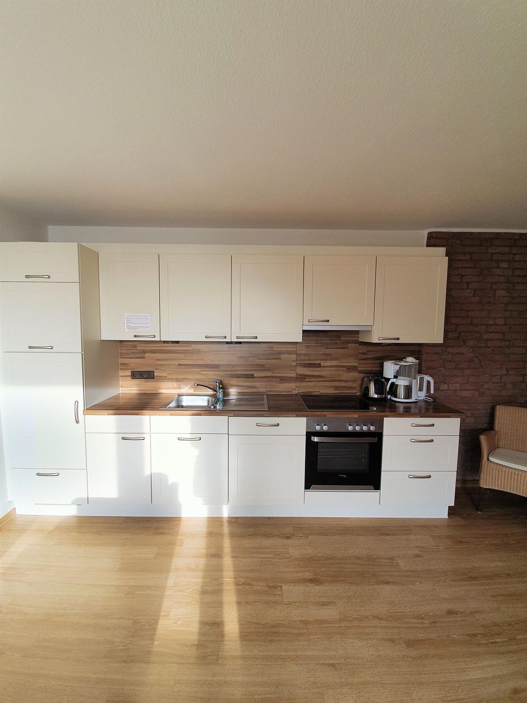 A modern kitchen with white cabinets, a wooden countertop, a built-in oven, and a coffee maker.