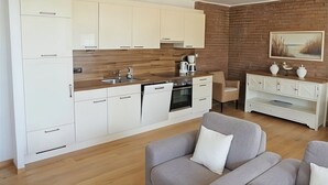 Una cocina moderna con armarios blancos, una encimera de madera y una pared de ladrillo. Hay una zona de comedor con un sofá gris y una mesa de centro blanca.