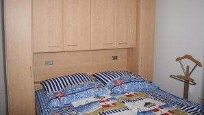 Una cama con colcha de motivos náuticos, un armario de madera arriba y una silla de madera con estructura metálica.