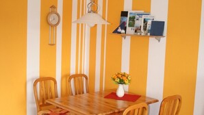 Un comedor con una mesa y sillas de madera, una lámpara colgante, un reloj y una estantería con libros y un jarrón de flores.