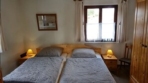 Ein Doppelbett mit zwei Nachttischen, ein Fenster mit Vorhängen, ein Holzschrank und ein Spiegel an der Wand.