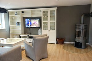 A modern living room with a television, white cabinets, a grey sofa, and a wood-burning stove. - Golfoase 2 - Semi-detached house for 6 people - Semi-detached house Golfoase 2 for 6 (Oevenum)