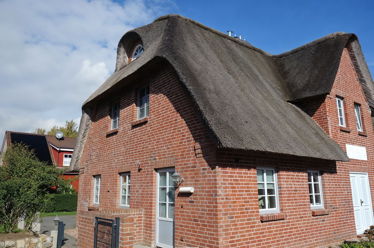 A red brick building with a steeply pitched thatched roof and a small window.