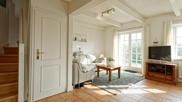 A living room with a sofa, coffee table, TV, and a staircase. - Triibergem 39 - DHH - Holiday home in Utersum: 75 m², garden, 500 m to the beach, (Utersum)