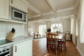 Une cuisine avec des meubles blancs, un four à micro-ondes, un bloc à couteaux et un coin repas avec des chaises et une table en bois.