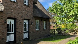 A brick building with a steeply pitched roof, multiple windows, and a paved driveway. - Triibergem 39 - DHH - Holiday home in Utersum: 75 m², garden, 500 m to the beach, (Utersum)