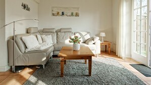 A living room with a sofa, a coffee table with a plant, a lamp, and a painting on the wall. - Triibergem 39 - DHH - Holiday home in Utersum: 75 m², garden, 500 m to the beach, (Utersum)