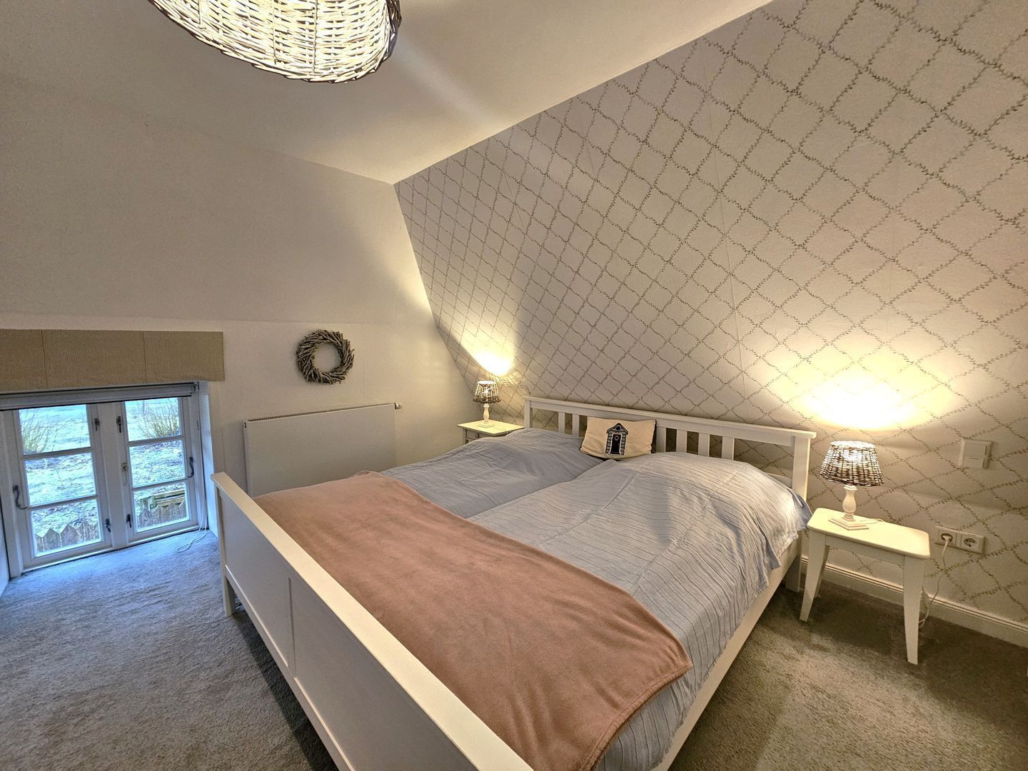 A bedroom with a bed, two bedside tables, a lamp, a window, and a door.