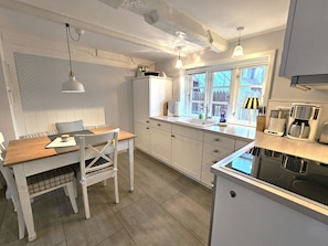 A modern kitchen with a dining area, white cabinetry, a window with a view, and a coffee maker. - WattLütt - Allergy-friendly WattLütt vacation apartment with terrace & parking space (Oevenum)