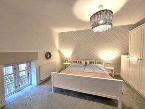 Une chambre à coucher comprenant un lit, deux tables de chevet, une armoire, une fenêtre avec vue et un luminaire suspendu.