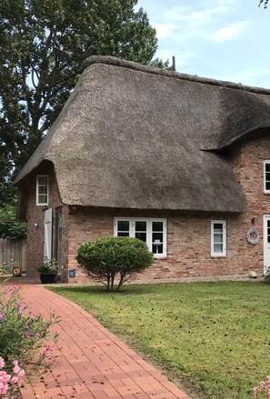 Une maison en briques avec un toit de chaume, un petit jardin et un chemin pavé.