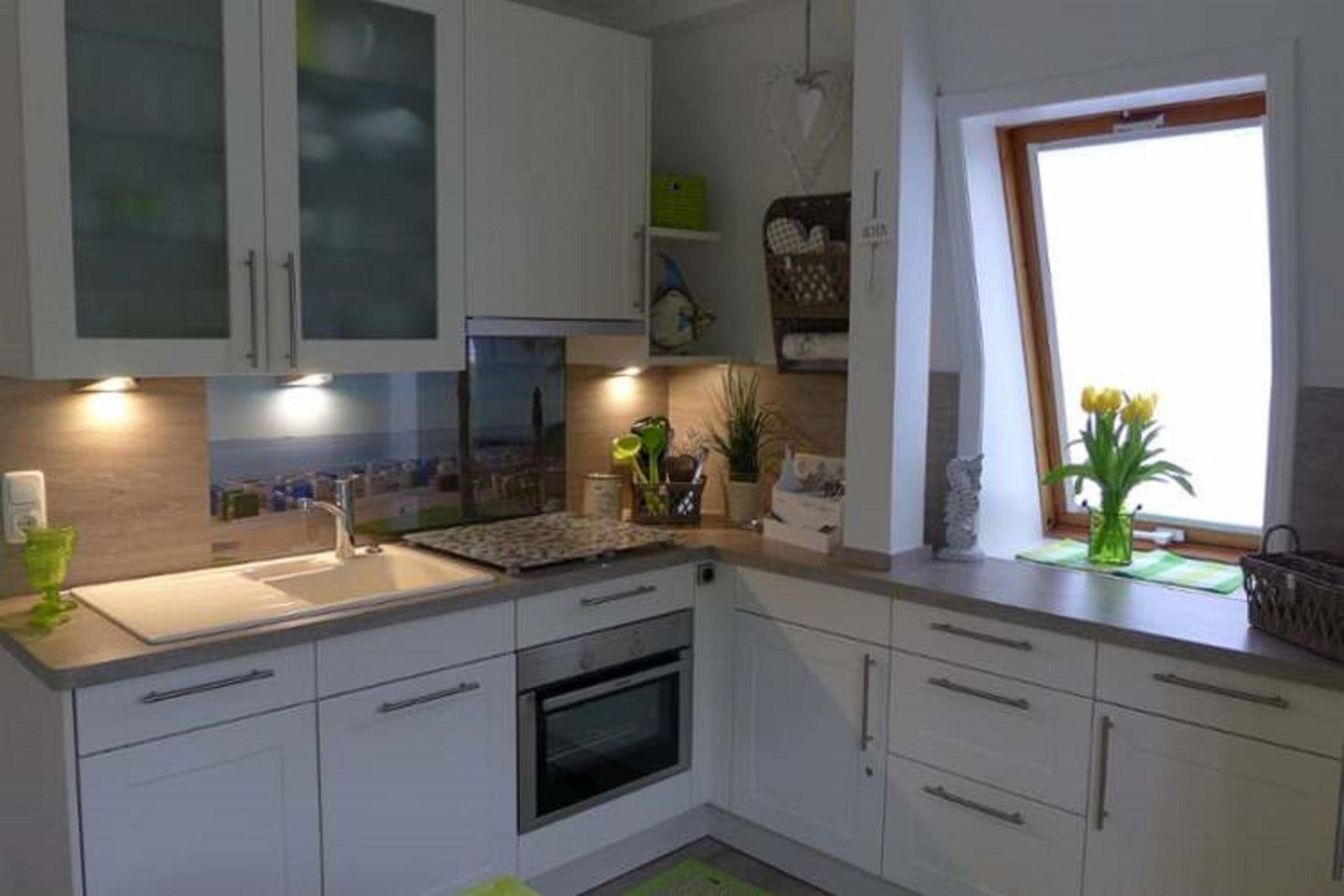 A modern kitchen with white cabinets, a built-in oven, a sink, and a window with a view.