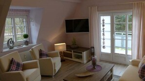 Ein Wohnzimmer mit einer Sofagarnitur, einem Couchtisch, einem an der Wand montierten Fernseher und einem Fenster mit Vorhängen.