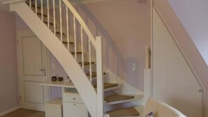 Eine Treppe mit weißen Geländern und Holzstufen, eine weiße Tür und ein kleiner, weißer Schrank mit Schubladen.