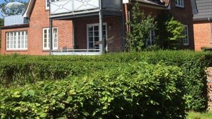 Ein zweistöckiges Backsteinhhaus mit Giebeldach, überdachter Veranda und einem sichtbaren Schornstein.